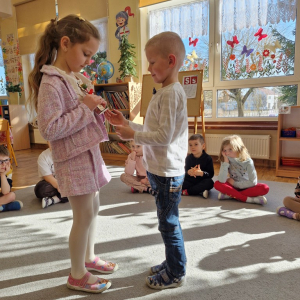 Chłopiec wręcza dziewczynce drewniany kwiatek z lizakiem z okazji Dnia Kobiet