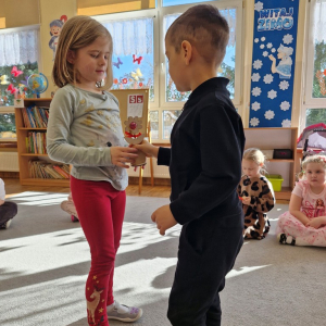 Chłopiec wręcza dziewczynce drewniany kwiatek z lizakiem z okazji Dnia Kobiet