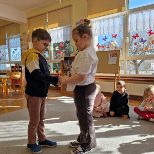 Chłopiec wręcza dziewczynce drewniany kwiatek z lizakiem z okazji Dnia Kobiet