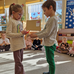 Chłopiec wręcza dziewczynce drewniany kwiatek z lizakiem z okazji Dnia Kobiet