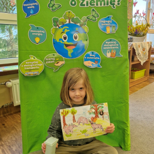 Dziewczynka prezentuje  pracę plastyczną "Wielkie porządki w lesie"