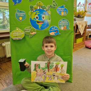 Chłopiec prezentuje  pracę plastyczną "Wielkie porządki w lesie"