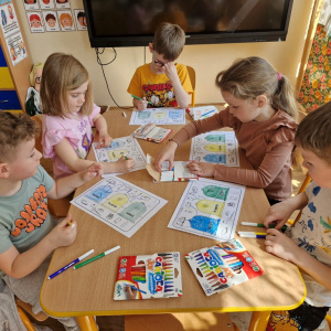 Dzieci w czasie pracy przy stoliku - wykonują zadanie w karcie pracy ( kolorują kosze i łączą obrazki przedstawiające odpady z  odpowiednimi pojemnikami) 
