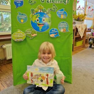 Chłopiec prezentuje  pracę plastyczną "Wielkie porządki w lesie"