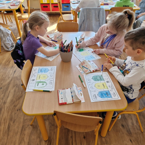 Dzieci w czasie pracy przy stoliku - wykonują zadanie w karcie pracy ( kolorują kosze i łączą obrazki przedstawiające odpady z  odpowiednimi pojemnikami) 