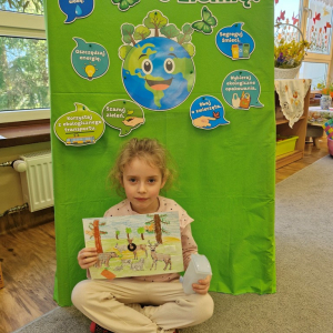 Dziewczynka prezentuje  pracę plastyczną "Wielkie porządki w lesie"