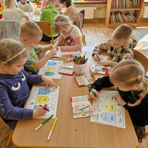 Dzieci w czasie pracy przy stoliku - wykonują zadanie w karcie prace ( kolorują kosze i łączą obrazki przedstawiające odpady z  odpowiednimi pojemnikami) 