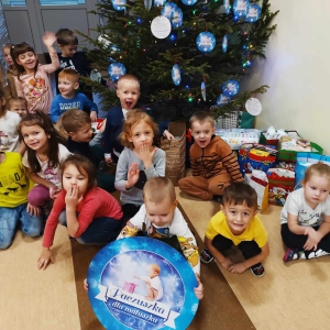 Przedszkolaki przekazujący dary w ramach akcji Paczuszka dla Maluszka pozujące na tle choinki