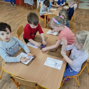 Dzieci siedzące przy stoliku ozdabiają papierowy szablon balona plasteliną
