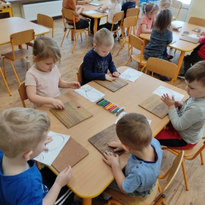Dzieci siedzące przy stoliku ozdabiają papierowy szablon balona plasteliną