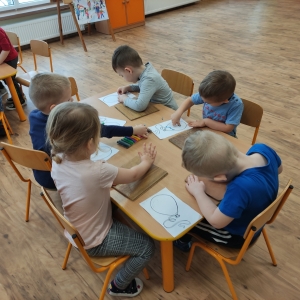 Dzieci siedzące przy stoliku ozdabiają papierowy szablon balona plasteliną